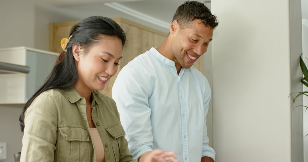 Diverse couple cooking together in modern kitchen, smiling while preparing meal