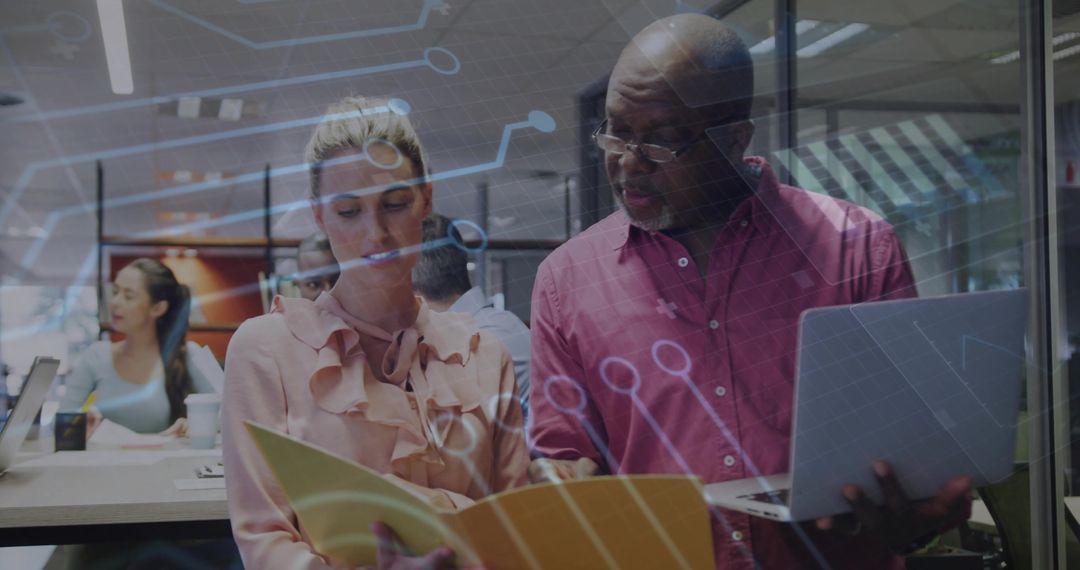 Mentor reviewing project with colleague using laptop and folder, digital circuit overlay