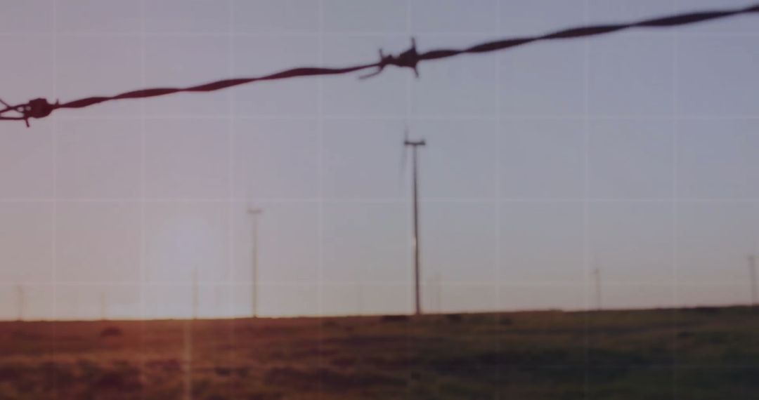 Barbed Wire Fencing with Sunset Over Open Landscape