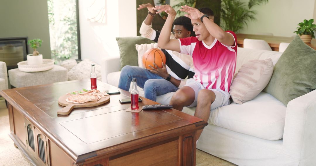 Two Friends Cheering on Couch with Basketball and Snacks at Home