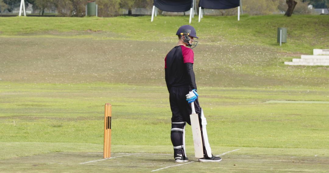 Cricketer Ready to Bat on Field with Equipment and Stumps in View
