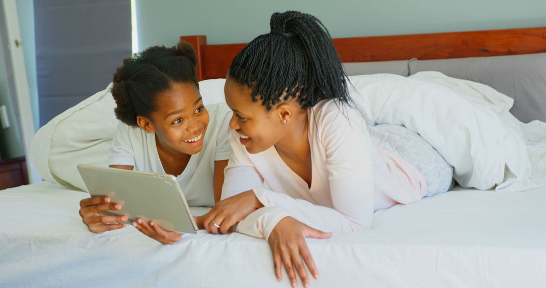 Two African American Girls Using Tablet Together on Bed Laughing - Free Images, Stock Photos and Pictures on Pikwizard.com