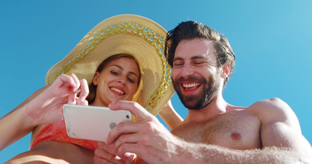 Cheerful Couple Enjoying Time Together on Beach with Smartphone - Free Images, Stock Photos and Pictures on Pikwizard.com