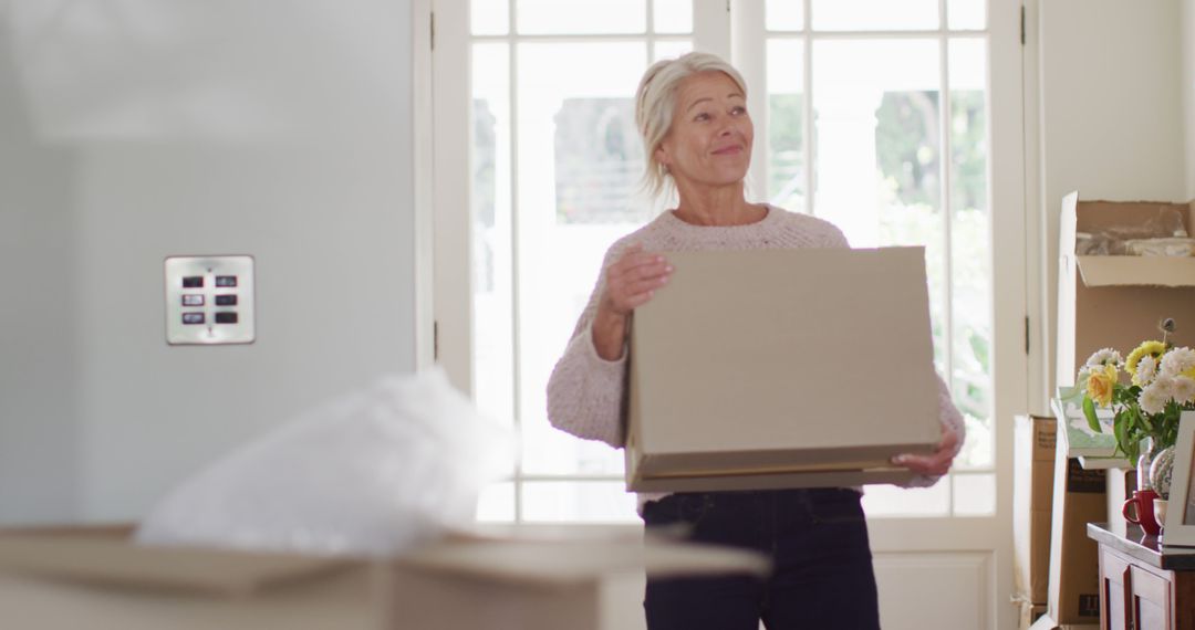 Senior woman moving into new home carrying cardboard box - Free Images, Stock Photos and Pictures on Pikwizard.com