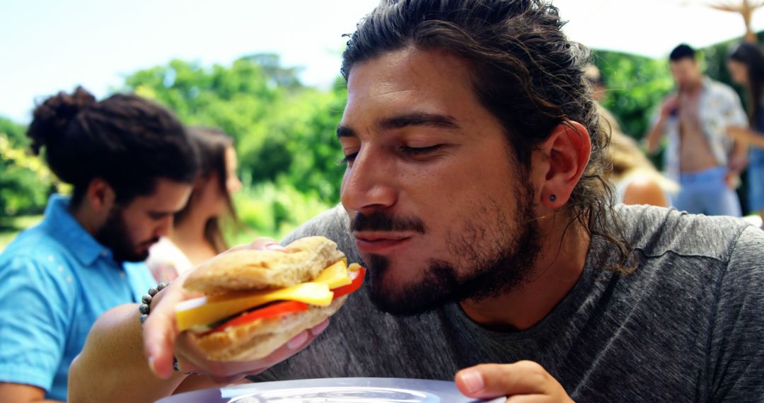 Man Enjoying a Sandwich at Outdoor Gathering - Free Images, Stock Photos and Pictures on Pikwizard.com