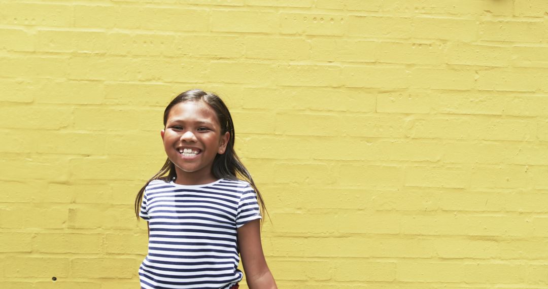Smiling Young Girl Against Yellow Brick Wall with Space for Text