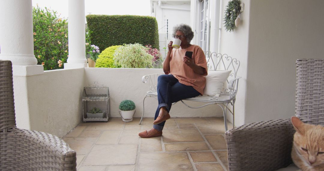 Senior woman relaxing on porch with a hot drink and newspaper, lovely cottage garden - Free Images, Stock Photos and Pictures on Pikwizard.com