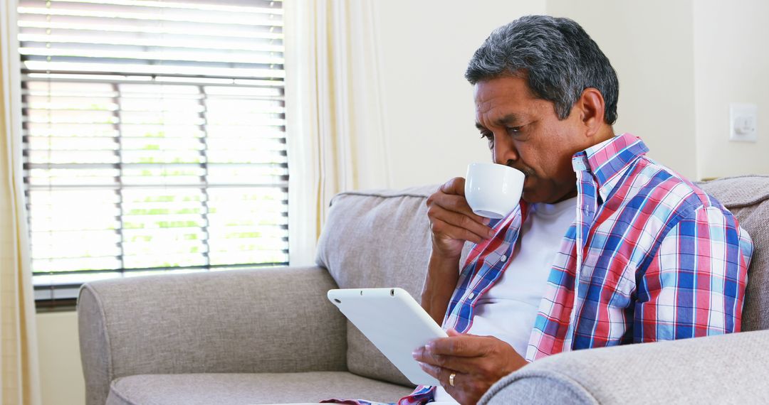 Senior Man Sitting on Sofa Drinking Coffee and Using Tablet - Free Images, Stock Photos and Pictures on Pikwizard.com