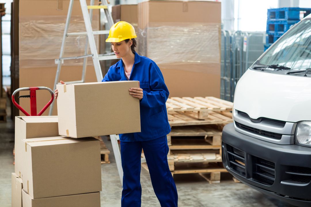 Warehouse Worker Transporting Boxes Near Van and Ladders