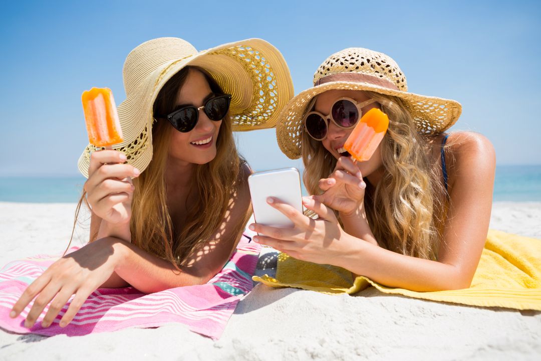 Female friends using smart phone while eating popsicles - Free Images, Stock Photos and Pictures on Pikwizard.com