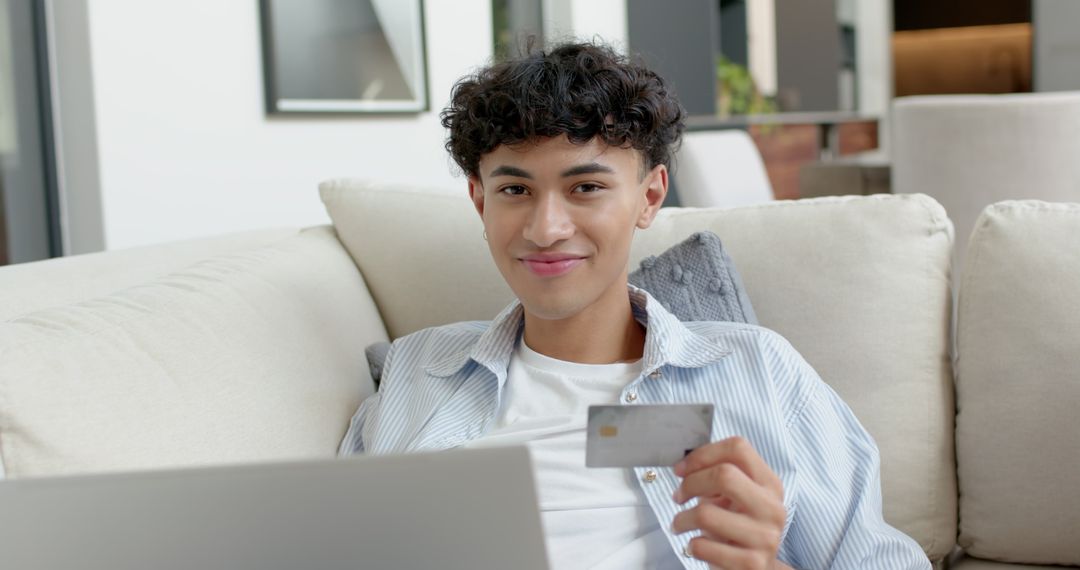 Young Man Shopping Online With Credit Card On Sofa