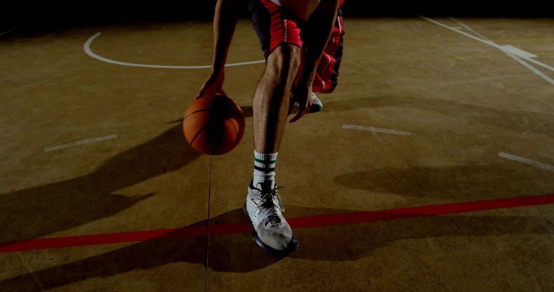 Low dribble basketball player on indoor court with red shorts and dramatic shadow
