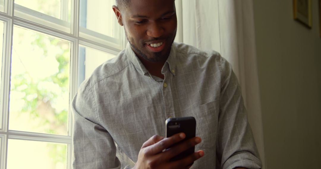 Smiling Man Using Smartphone by Bright Window - Free Images, Stock Photos and Pictures on Pikwizard.com