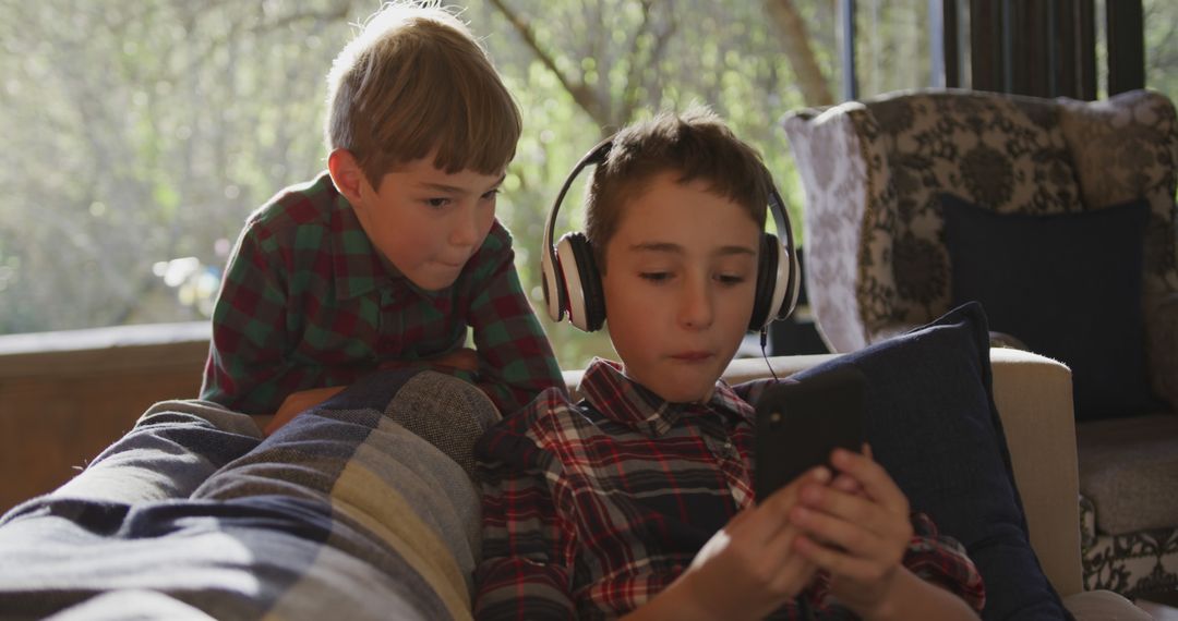 Two Boys Playing on Mobile Device with Headphones in Cozy Living Room - Free Images, Stock Photos and Pictures on Pikwizard.com