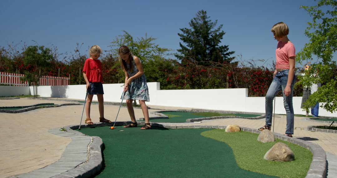 Teen Girls Enjoying Outdoor Mini-Golf Game On Sunny Day