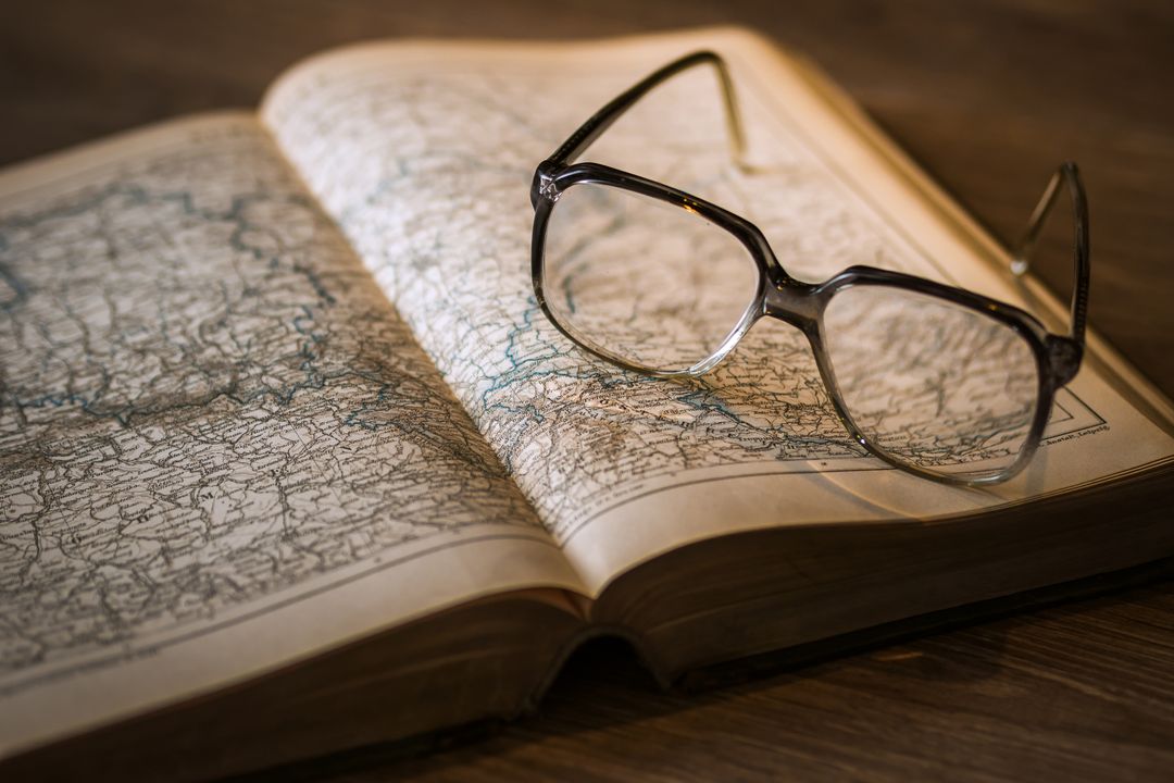 Antique atlas with reading glasses resting on open map for travel study inspiration