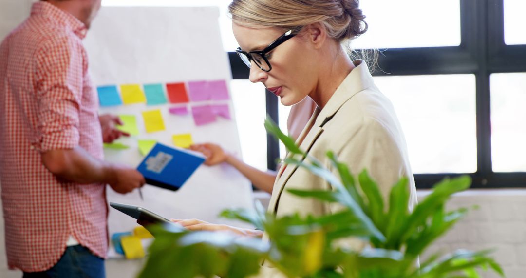 Businesswoman Using Tablet in Office Meeting with Sticky Notes on Wall - Free Images, Stock Photos and Pictures on Pikwizard.com