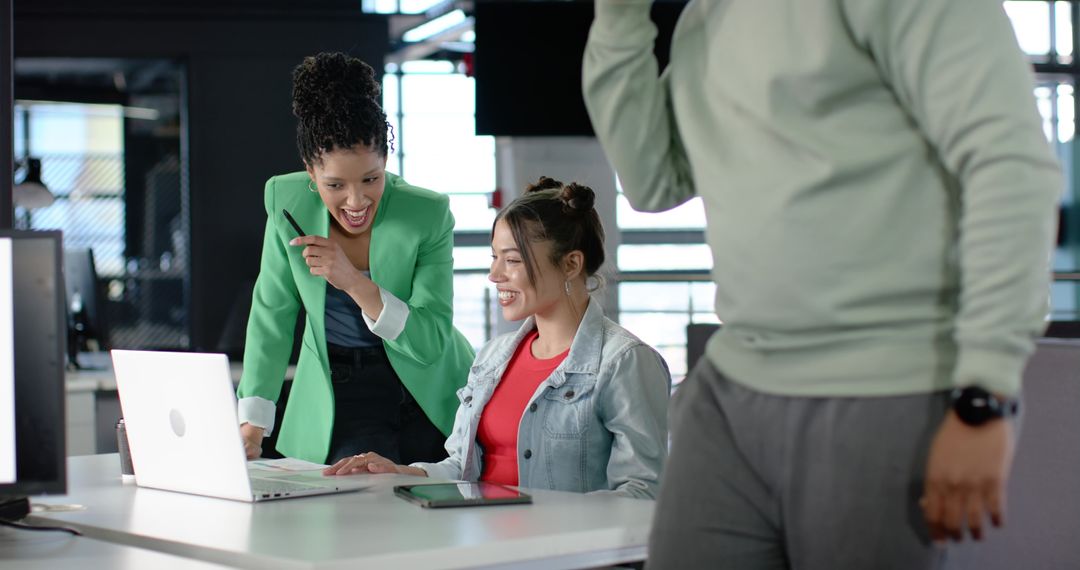 Indian coworker pointing at laptop while collaborating with colleague in modern office