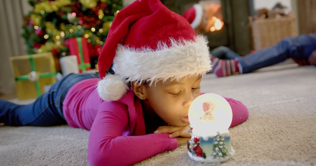 Child Wearing Santa Hat with Snow Globe in Christmas Living Room - Free Images, Stock Photos and Pictures on Pikwizard.com