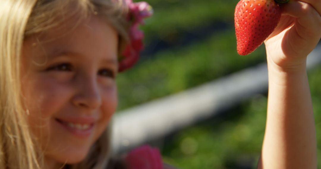 Caucasian girl examines a strawberry outdoors, with copy space - Free Images, Stock Photos and Pictures on Pikwizard.com