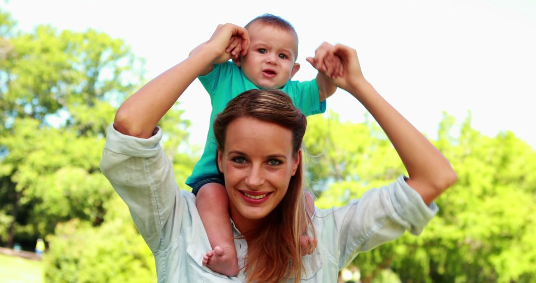 Smiling Mother Holding Baby on Shoulders in Park - Free Images, Stock Photos and Pictures on Pikwizard.com