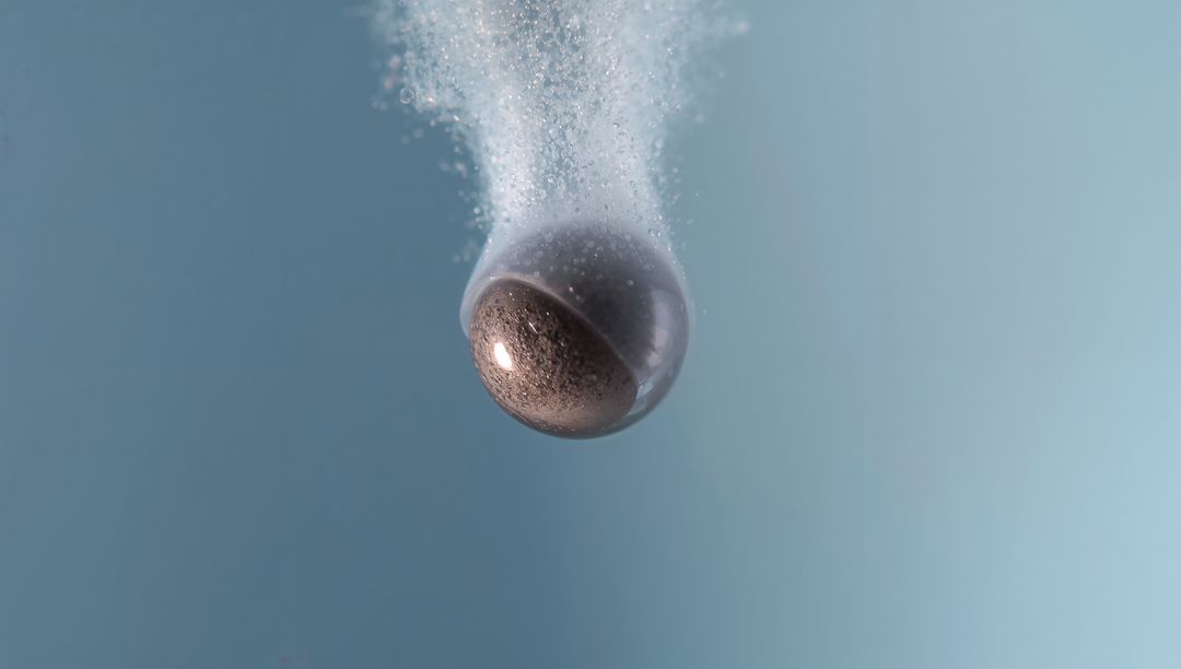 Floating glass sphere with half-rough bronze core releasing microbubbles in aqua liquid