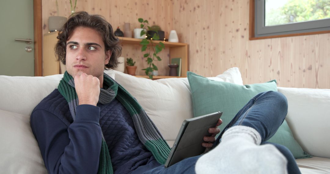 Young Man Relaxing on Sofa Using Tablet in Modern Minimalist Home