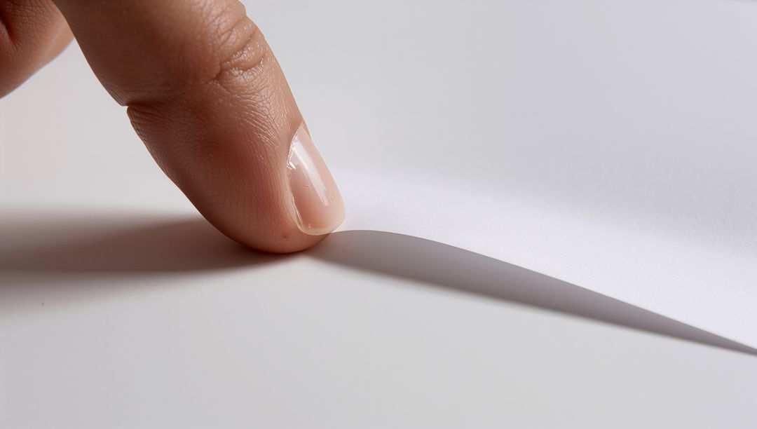 Fingertip Lifting Curled Corner of White Paper Casting Soft Shadow, Minimal Macro Detail