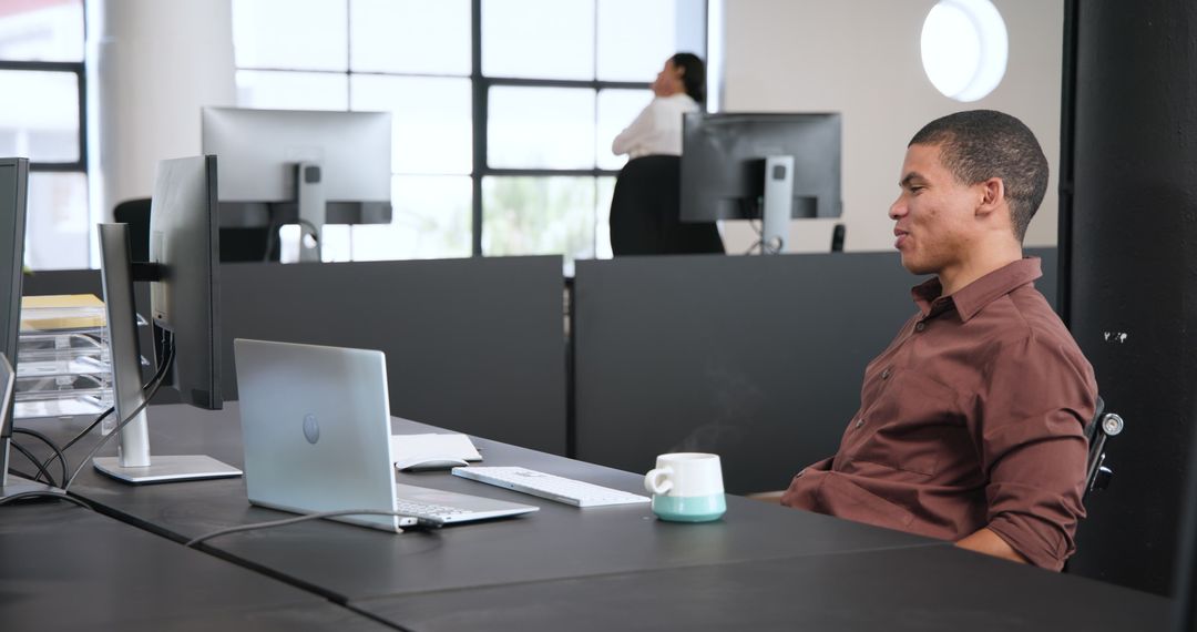 Businessman Working at Laptop with Colleague on Phone in Open Office Space