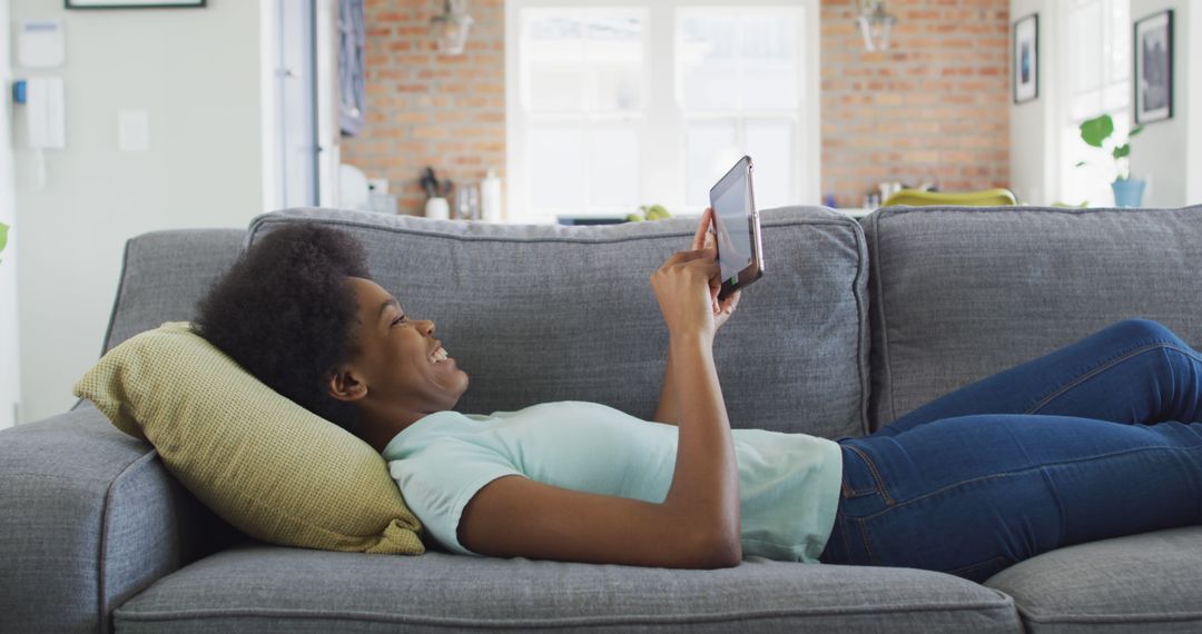 African American Woman Relaxing at Home and Using Tablet on a Sofa - Free Images, Stock Photos and Pictures on Pikwizard.com