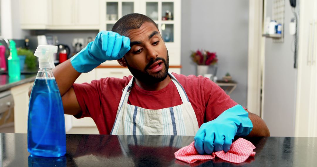 Tired Man Cleaning Kitchen Counter Wearing Gloves and Apron - Free Images, Stock Photos and Pictures on Pikwizard.com