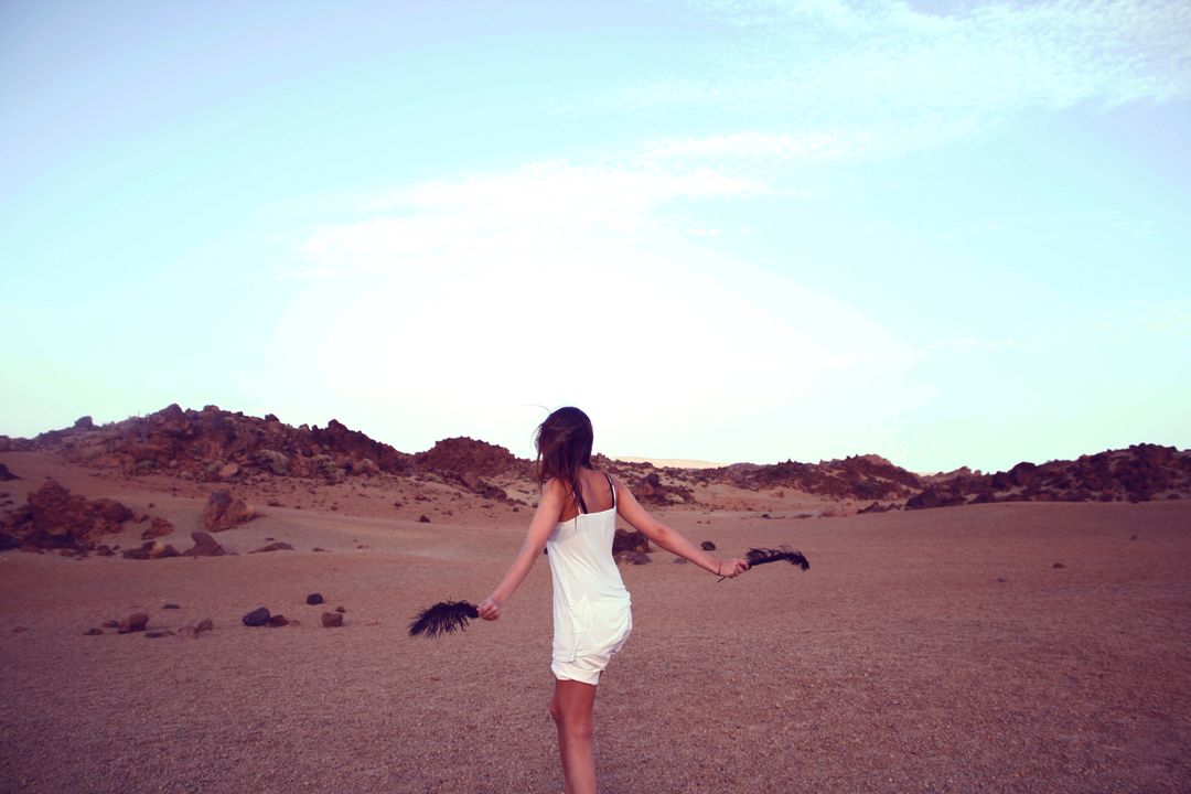 Woman in White Dress Holding Feathers in Desert Landscape - Free Images, Stock Photos and Pictures on Pikwizard.com