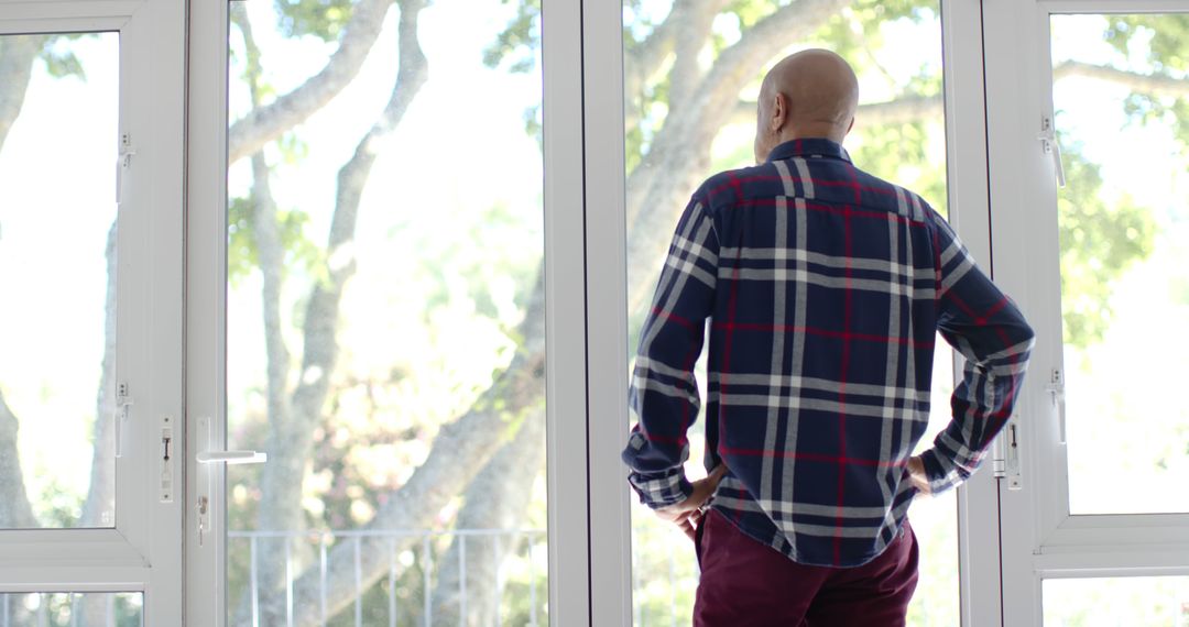 Serene Man in Checked Shirt Looking Out Window at Trees - Free Images, Stock Photos and Pictures on Pikwizard.com