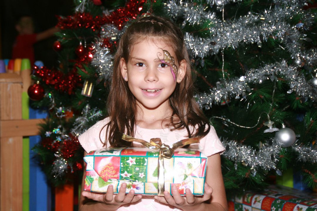 Smiling Girl Holding Gift Near Decorated Christmas Tree - Free Images, Stock Photos and Pictures on Pikwizard.com