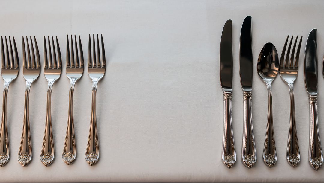Polished Silverware on White Tablecloth Showing Symmetrical Forks and Knives for Tabletop