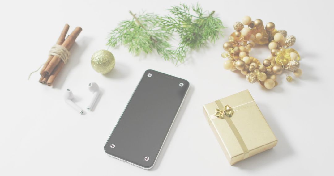 Minimalist festive flatlay featuring smartphone, gold gift box, pine sprig, wreath, cinnamon