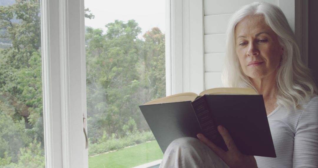 Senior Woman Reading Book by Sunny Window, Relaxing Afternoon - Free Images, Stock Photos and Pictures on Pikwizard.com