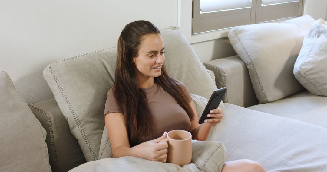 Relaxed Woman using Smartphone on Sofa with Coffee Mug