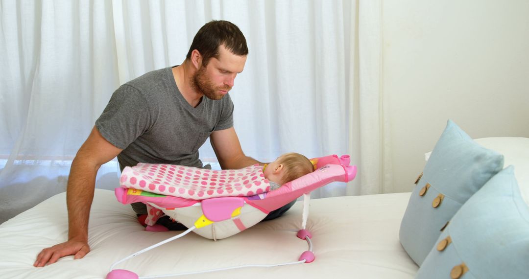 Caring Father Watching Over Resting Baby in Bouncer on Bed - Free Images, Stock Photos and Pictures on Pikwizard.com