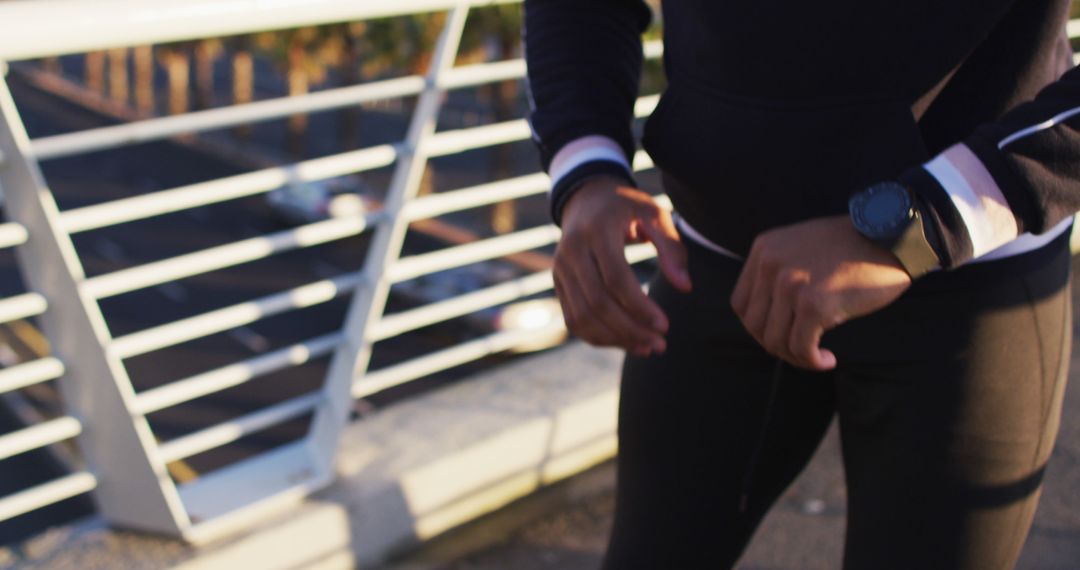 Midsection of african american man exercising on footbridge in city, checking smartwatch - Free Images, Stock Photos and Pictures on Pikwizard.com