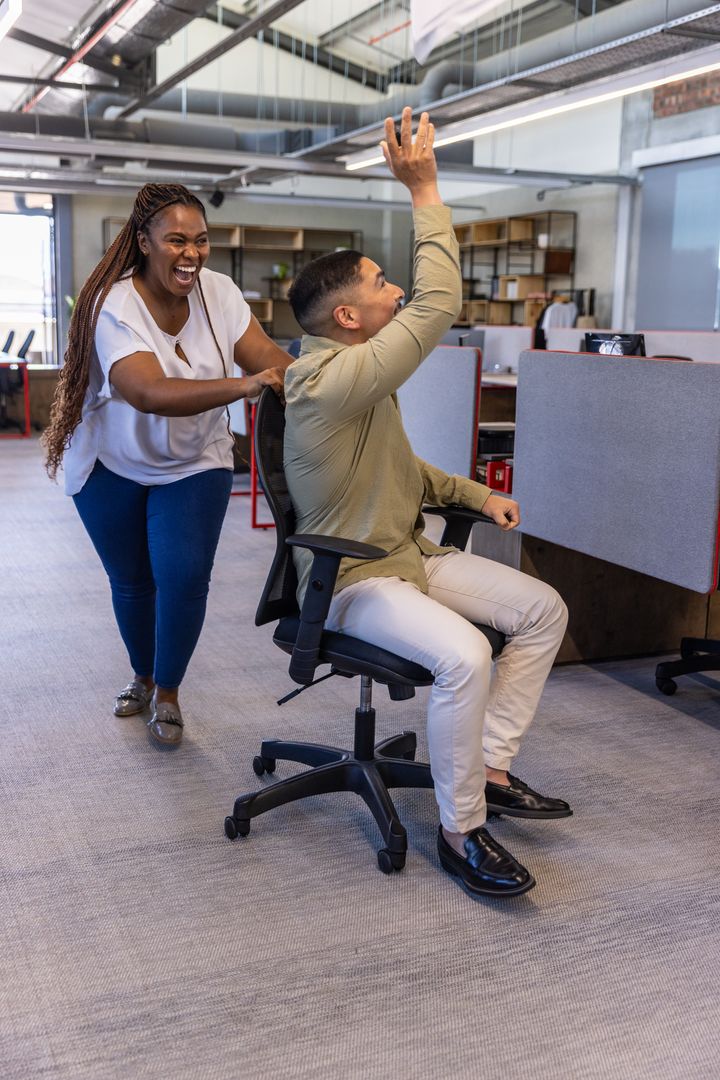Diverse Coworkers Enjoying Fun Moment at Office with Chair Ride