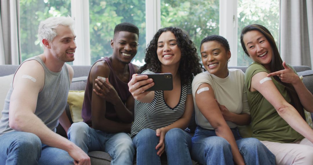 Diverse Friends Smiling While Showing Bandages and Taking a Selfie on Couch - Free Images, Stock Photos and Pictures on Pikwizard.com