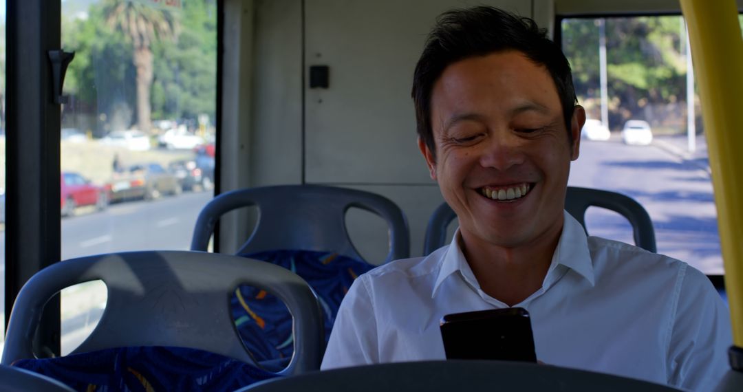 Asian Man Smiling on Bus Engaged with Smartphone, Morning Commute