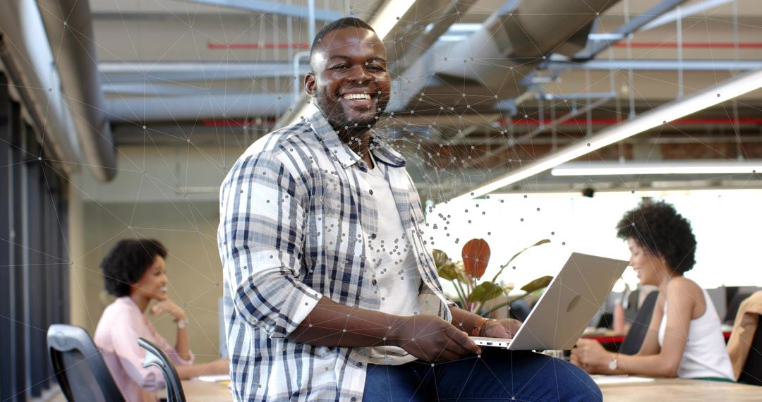 Smiling Black man holding laptop and working in bright modern coworking space