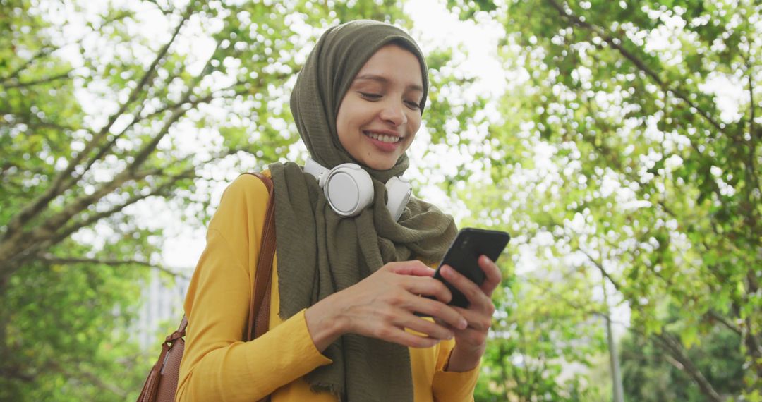 Smiling Muslim Woman Using Smartphone in Park, Outdoor Relaxation - Free Images, Stock Photos and Pictures on Pikwizard.com