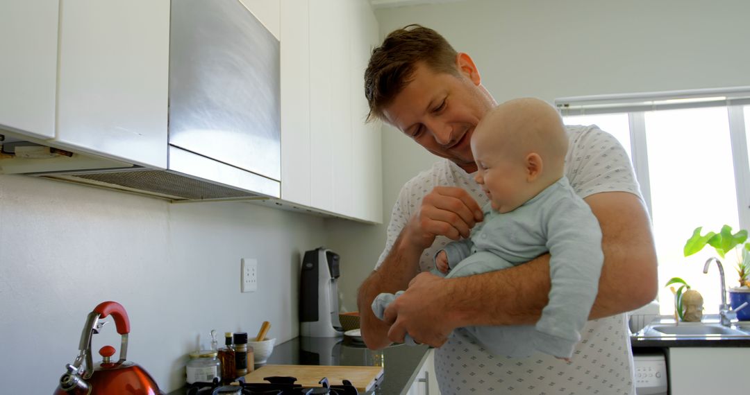 Father Holding Baby in Kitchen Playing and Smiling - Free Images, Stock Photos and Pictures on Pikwizard.com