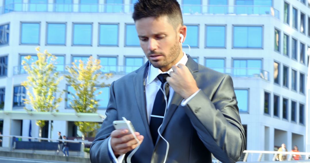 Businessman Using Smartphone with Earphones in Urban Setting - Free Images, Stock Photos and Pictures on Pikwizard.com