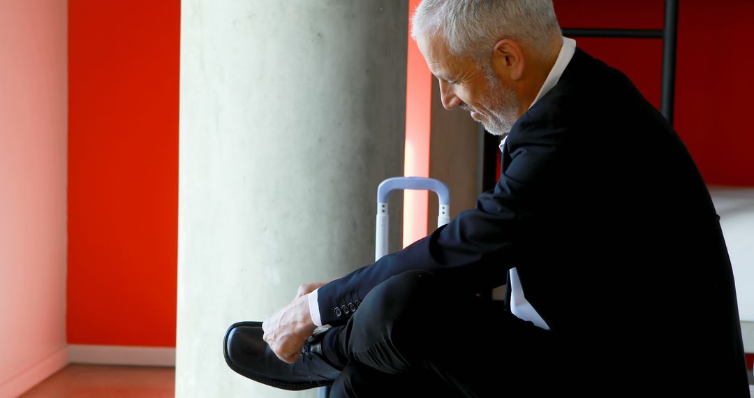 Caucasian businessman ties his shoe in an office setting - Free Images, Stock Photos and Pictures on Pikwizard.com