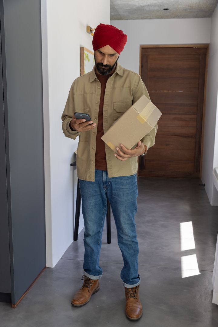 Man in Casual Attire Checking Smartphone While Holding Package