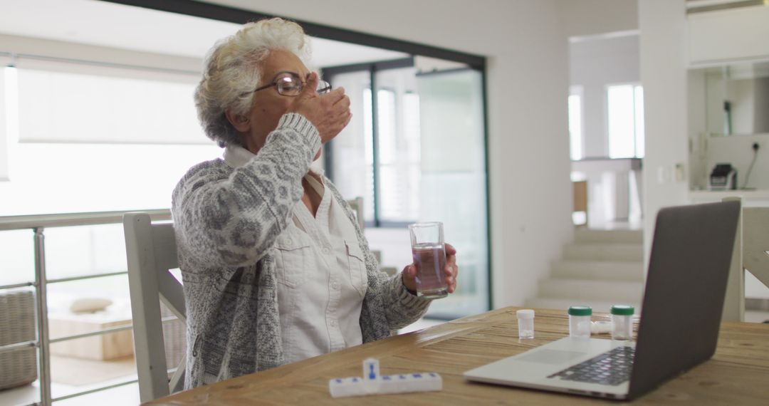 Elderly Woman Takes Medication While Using Laptop at Home - Free Images, Stock Photos and Pictures on Pikwizard.com